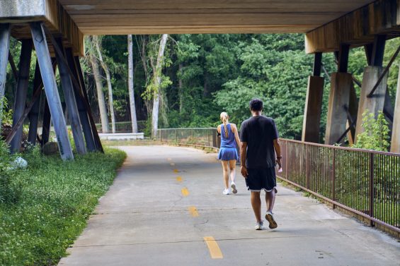 View of back of two people on a recreational walk under a bridge in an Alpharetta park.